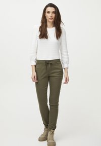 Pantalons de jogging verts olive avec taille à cordon ajustable, associés à un haut blanc texturé à manches longues avec des manches bouffantes.
