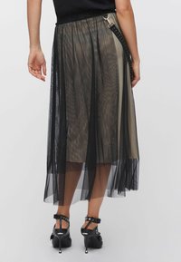 Gonna in rete nera con design trasparente, caratterizzata da un pannello opaco a contrasto. Include una fascia in vita e cinturini decorativi con borchie.