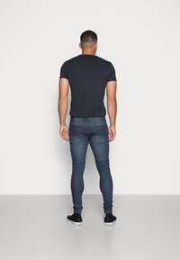 Mörk åtsittande t-shirt, blå skinny jeans och svarta sneakers. Slät textur, avslappnad design, synliga sömmar på jeansen och slätt tyg.