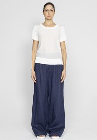 Biała koszula z krótkim rękawem o przezroczystej fakturze i jednolitym dołem, zestawiona z luźnymi granatowymi spodniami lnianymi i białym obuwiem.