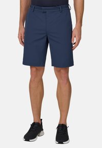 Pantaloncini blu navy realizzati in tessuto leggero, con fronte piatto, passanti per cintura e orlo rifinito. Indossati con scarpe da ginnastica nere.