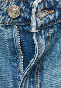 Denim jeans with a light blue wash, featuring a metal button closure and a zipper fly. Visible stitching details with a slight distressed texture.