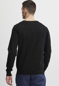 Svart strikket genser med lange ermer, klassisk rund halsutringning, og ribbestrikkede mansjetter og kant. Glatt tekstur, middel tykkelse.