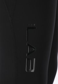 Zwarte sportlegging met een gladde textuur, voorzien van een verticale "ELITE LAB"-logo in glanzende afwerking langs de zijnaad. Zichtbare naden.
