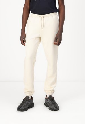 Cream-colored sweatpants with elastic cuffs and drawstring waist. Paired with dark, textured sneakers. Simple design without patterns.