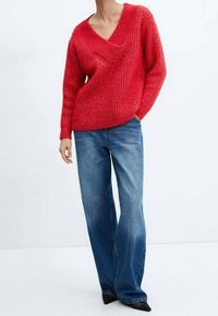 Pull rouge en tricot avec un décolleté en V profond et un motif texturé. Associé à un jean large bleu clair et des chaussures noires à bout pointu.