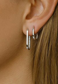 Orecchini a cerchio in argento, caratterizzati da un design elegante, con uno di essi impreziosito da piccoli cristalli trasparenti, appesi a un lobo vicino a capelli lisci.