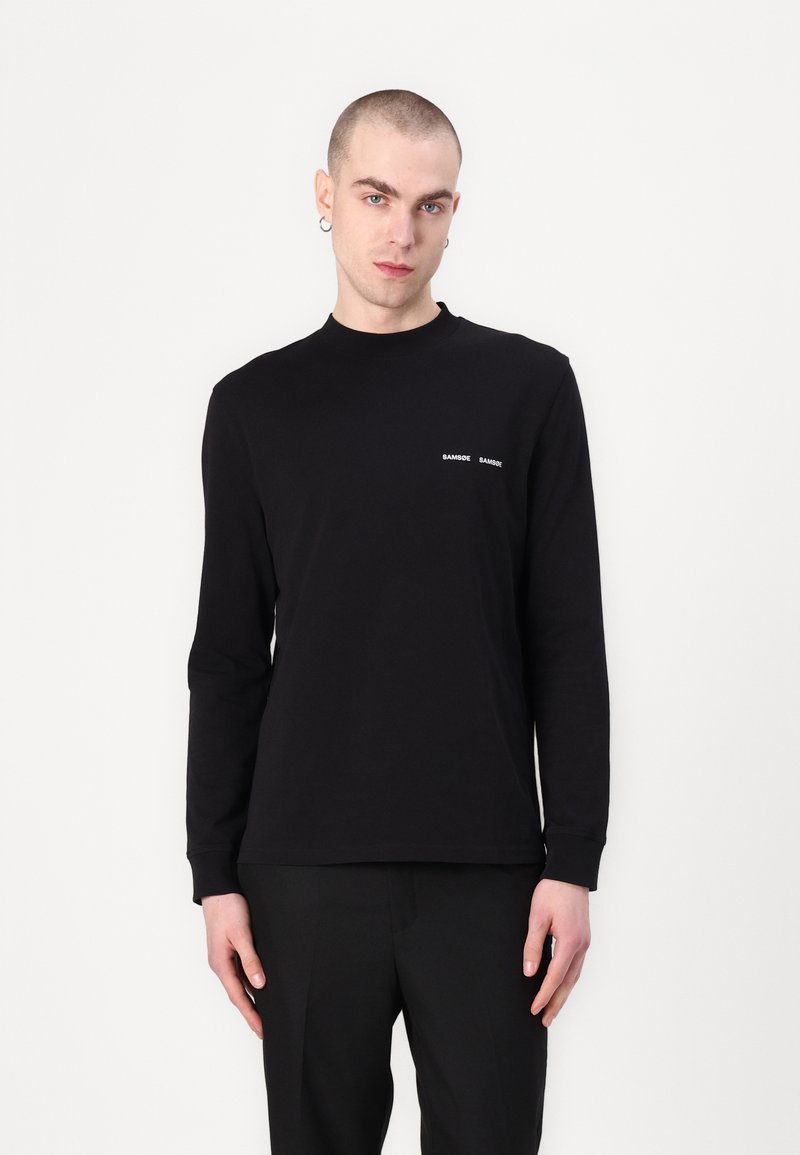 Black long-sleeve shirt made of cotton, featuring a round neckline and minimalistic white text logo on the chest. Smooth texture.