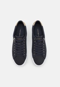 Navy canvas sneakers with gold-tone accents and round laces, featuring a white rubber sole and brand logo printed on the insole.