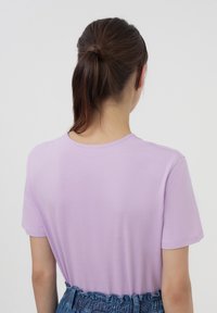 T-shirt lilla a maniche corte con scollatura tonda, texture liscia e vestibilità rilassata, abbinato a una cintura blu con texture.