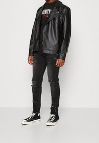 Musta nahkainen moottoripyörätakki, musta graafinen t-paita, mustat revityt tiukat farkut ja mustat kangasvalkoiset korkeavartiset tennarit.