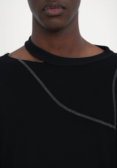 Schwarzes Top mit asymmetrischem Ausschnitt, das kontrastierende graue Nähte entlang einer geschwungenen Naht und einen rohen Saum aufweist. Weicher Stoff.