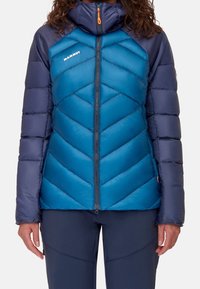Giacca isolante blu e navy con motivo a zigzag, collo alto, zip completa e logo sul petto. Texture liscia e design gonfio.