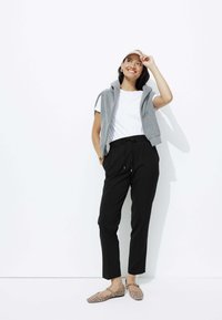 Un hoodie sans manches gris sur un t-shirt blanc, associé à un pantalon noir cintré et des ballerines à imprimé léopard, le tout sur un fond blanc.