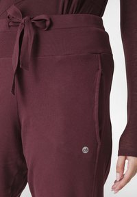 Bordeaux joggers met een geribbelde tailleband en strikdetail. Voorzien van zijzakken en een klein logo op het linkerbeen. Zachte stoftextuur.