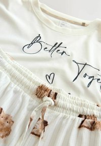 Weißes Baumwolloberteil mit schwarzem Schriftzug "Better Together" und einem Rock mit hellen Streifen und Tiermustern, mit elastischem Bund und Kordelzug.