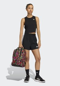 Top corto nero, pantaloncini neri e scarpe da ginnastica nere. Completa il look uno zaino multicolore con motivo floreale e dettagli verdi.