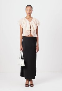 Blouse en pêches à volants avec un nœud à l'avant, associée à une jupe noire longueur sol. Un sac à main blanc et des sandales noires complètent le look.