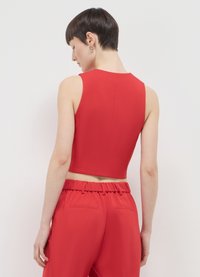 Haut court sans manches rouge en tissu lisse, avec un col montant, une coupe ajustée et un dos épuré avec des coutures minimales.