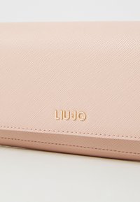 Lys rosa lommebok laget av teksturert materiale, med gull "LIU JO" branding og synlige sømmer langs kantene.