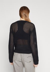 Schwarzer Strickpullover mit lockerem, offenem Netzmuster und gerippten Bündchen. Verfügt über einen Rundhalsausschnitt und eine entspannte Passform. Hinteransicht gezeigt.