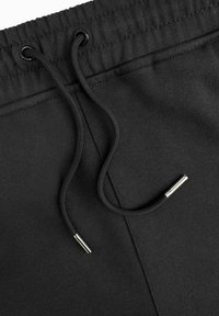 Zwarte sweatpants met een elastische tailleband en een koord. Heeft een gladde textuur en metalen aglets op het koord.