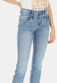 Jasnoniebieskie dżinsy o slim fit, pięć kieszeni i kontrastowe przeszycia. Posiadają dwa guziki z przodu oraz średni stan.