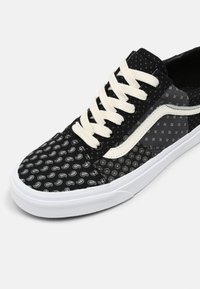 Baskets noires avec tissu à motifs paisley, lacets crème, semelle en caoutchouc blanche et accents gris sur les côtés.