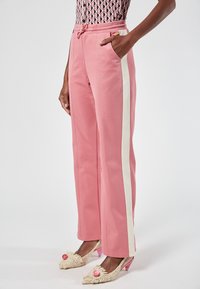 Rosa Jogginghosen mit weißen Seitstreifen, elastischem Bund und Taschen, kombiniert mit gehäkelten Absätzen in Rosa.