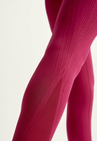 Leggings i livlig rosa med texturerat mönster. Har en elegant design och slät finish som framhäver kroppens konturer och tygens rörelse.