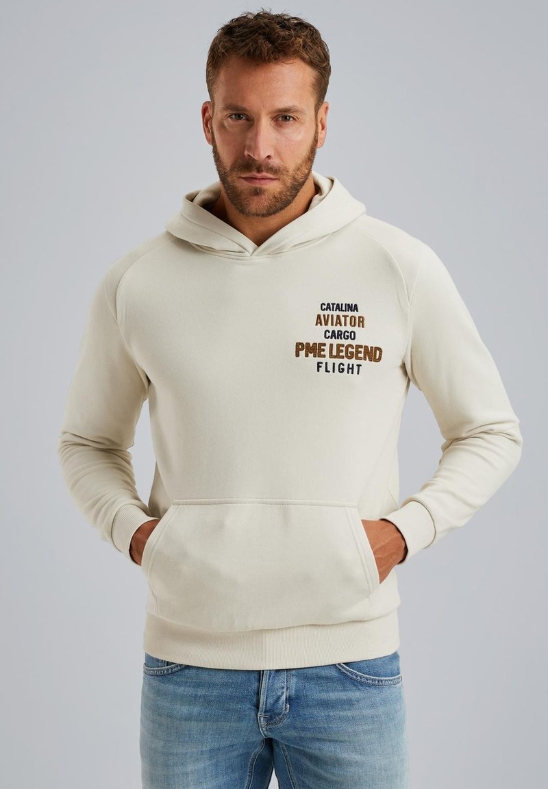 Beige hoodie met een kangoeroezak, ribgebreide manchetten en geborduurde tekst in bruin en zwart. Zacht materiaal, ontspannen pasvorm, casual ontwerp.