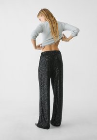 Sorte pailletterede bukser med bred benvidde og en strækbar talje. En lys grå ribbet sweater er delvist stoppet ind bagpå.