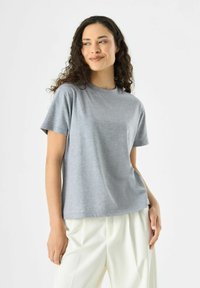Graues kurzärmliges T-Shirt aus leichtem, strukturiertem Stoff mit rundem Ausschnitt und lockerer Passform, kombiniert mit hellen Hosen.