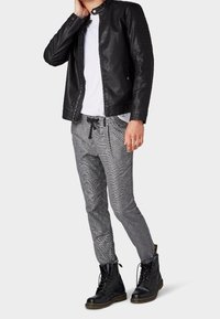 Czarna skórzana kurtka z wysokim kołnierzem, szare spodnie w deseń oraz czarne sznurowane botki. Tkanina ma wzór jodełki i dopasowany krój.