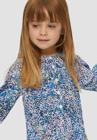Kinderjurk gemaakt van lichtgewicht stof; heeft een abstract patroon in paars, blauw en groen, lange mouwen en een knoopsluiting aan de voorkant.