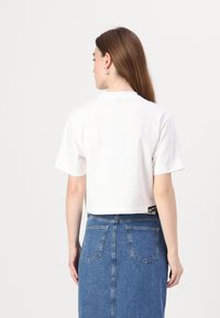 Bela, skrajšana majica s kratkimi rokavi in okroglim ovratnikom, v kombinaciji z modrim jeans krilom visoke pasu, ki ima vidne žepke.