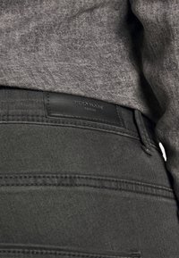 Svarta denim jeans med en texturerad finish, med en svart läderetikett märkt "VERO MODA" vid bakre midjan och minimala sömdetaljer.