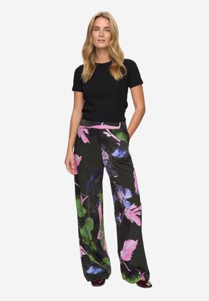 Bukser med vide ben i blomstermønster med levende nuancer af pink, grøn og blå mod en sort baggrund, kombineret med en tætsiddende sort t-shirt.