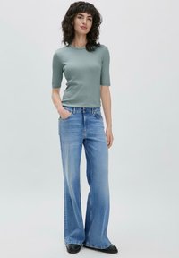 Harmaa lyhythihainen paita yhdistettynä vaaleansinisiin leveälahkeisiin farkkuihin. Farkuissa on klassinen viiden taskun malli ja suora vyötärö.