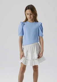 Top azzurro chiaro a costine con maniche a palloncino, abbinato a una gonna bianca a più strati. La gonna presenta un orlo ondulato e delicati dettagli a occhio di pernice.