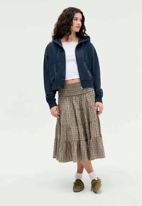 Hanorac scurt bleumarin, top alb moulant și fustă în straturi cu carouri în tonuri de bej și maro. Pantofi maronii, sosete albe și croială lejeră.