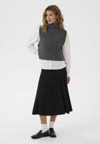 Sivi pleteni prsluk s visokim ovratnikom, nošen preko bijele košulje s dugmadi ukrašene malim plavim točkicama, u kombinaciji s crnom suknjom i cipelama.