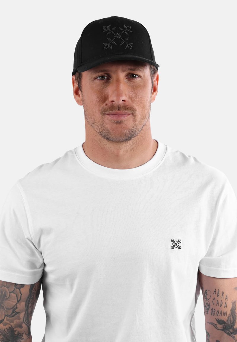 T-shirt blanc avec un col rond et des manches courtes, affichant un petit logo noir sur la poitrine gauche. Casquette noire avec un design brodé.