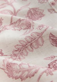 Tissu avec des motifs floraux et de feuilles rose pâle sur une étoffe texturée blanc cassé, montrant des plis et des détails finement tissés.