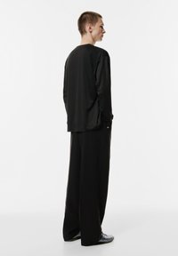 Schwarzes Langarmoberteil mit lockerer Passform, kombiniert mit weiten schwarzen Hosen. Glatte Stoffqualität mit schlichtem Design und minimalen Akzenten.