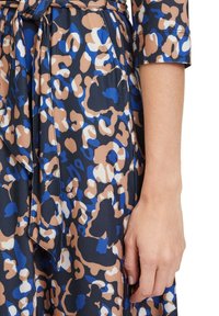 Leopardmönstrad klänning i nyanser av blått, beige och marinblått. Tillverkad av ett mjukt tyg med knytband i midjan. Har en design med 3/4-långa ärmar.