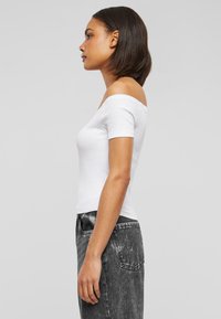 Balta off-the-shoulder krekls ar īsām piedurknēm, pieguļošs dizains, kombinēts ar augsto vidukli melniem džinsiem ar izbalējušu rakstu.