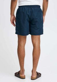 Pantaloni corti blu navy con cintura elastica, tasche laterali e una tasca posteriore. Realizzati in tessuto leggero, con una superficie liscia.