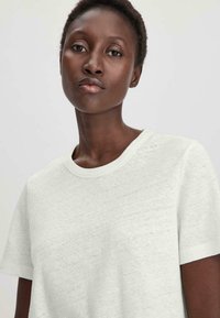 T-shirt blanc à manches courtes, fabriqué en tissu doux et texturé, avec un col rond et des détails de couture visibles.