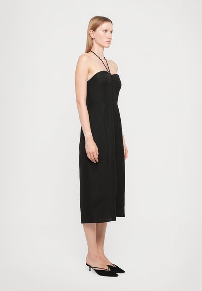 Black strapless dress with a straight cut, featuring a button-down front and smooth texture. Paired with black heeled mules.